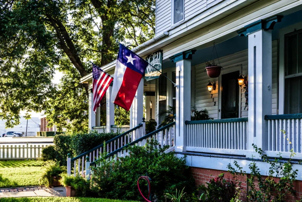 A Texas house with a large porch and both the US and Texas state flags flying on the front.