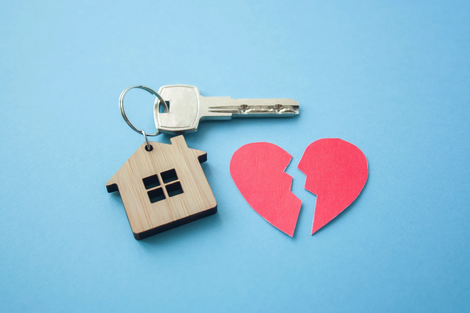 A house key with a house-shaped keychain and a broken heart, suggesting an issue with divorce and property.